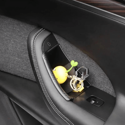 Rangement de portière avec porte-clés et accessoires dans une voiture Tesla, alliant style et fonctionnalité.