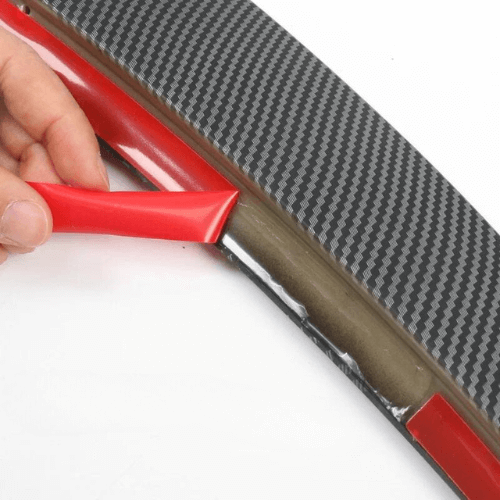 Close-up of a hand applying adhesive to a Tesla Model 3 spoiler, showcasing its carbon fiber design.