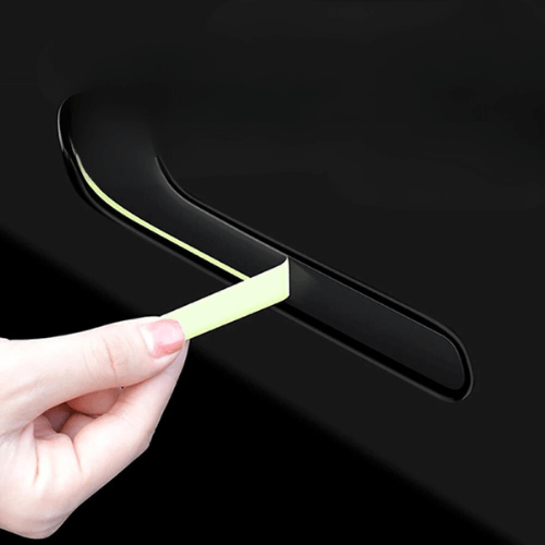 Person applying a covering to the door handle of a Tesla Model 3 for enhanced protection and aesthetics.