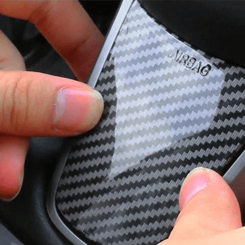 Close-up of hands applying carbon fiber wrap to a Tesla steering wheel for enhanced grip and style.