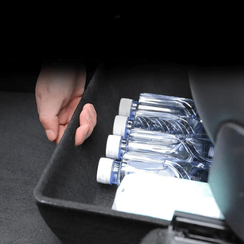 Bac de rangement sous siège avec bouteilles d'eau dans un Tesla Model Y, optimisant l'espace disponible.