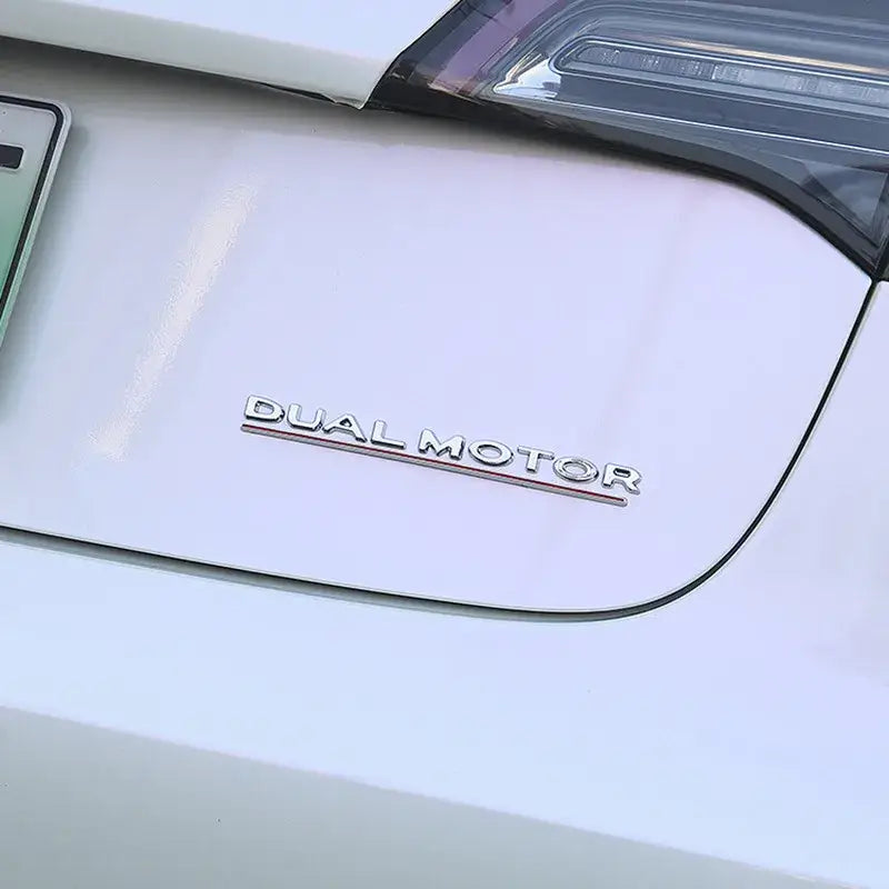 Metallic Dual Motor emblem on a white Tesla vehicle, showcasing modern elegance and Tesla community pride.