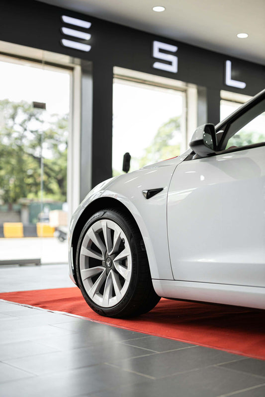 Tesla sur un tapis rouge dans une salle d'exposition, prêt pour être équipé d'accessoires incontournables pour une expérience de conduite optimale.